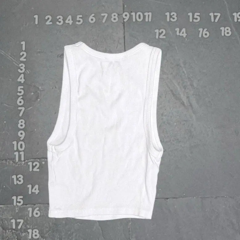 White tank top on a gray textured background with measurement scale