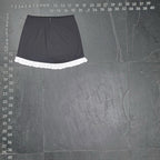 The Room Collective black mini skirt with white ruffled hem. High-waisted, slim fit, polyester/spandex blend with cotton ruffle. Back zipper.