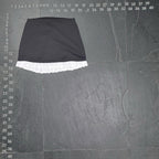 The Room Collective black mini skirt with white ruffled hem. High-waisted, slim fit, polyester/spandex blend with cotton ruffle. Back zipper.