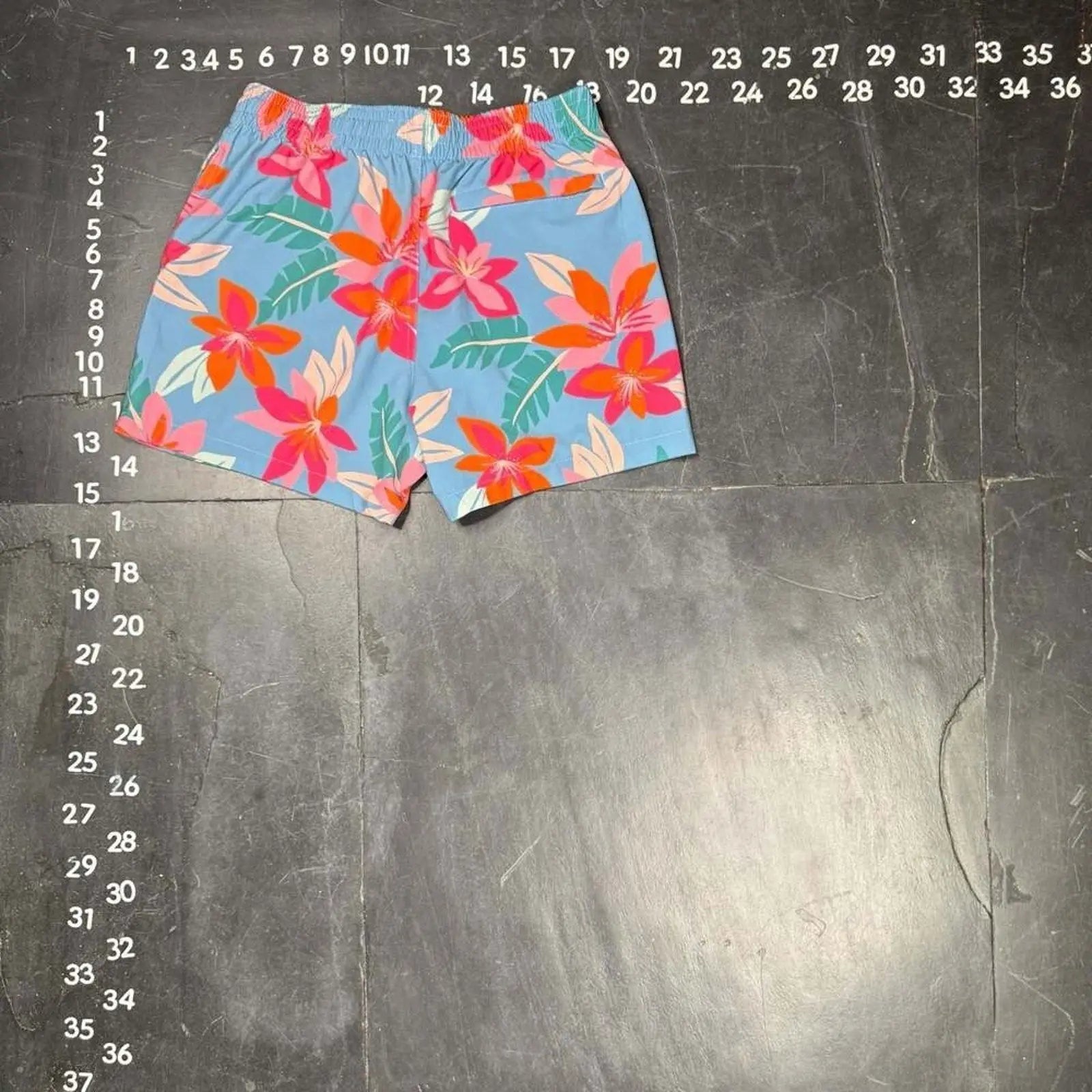 The Room Collective light blue floral print swim trunks for men, size small, with pink and orange hibiscus flowers.
