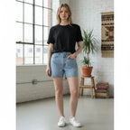 The Room Collective light wash high rise denim shorts with five-pocket styling and zip fly, worn by a model.