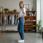 The Room Collective: Mid-blue denim bootcut jeans on a woman wearing a white t-shirt and white sneakers.