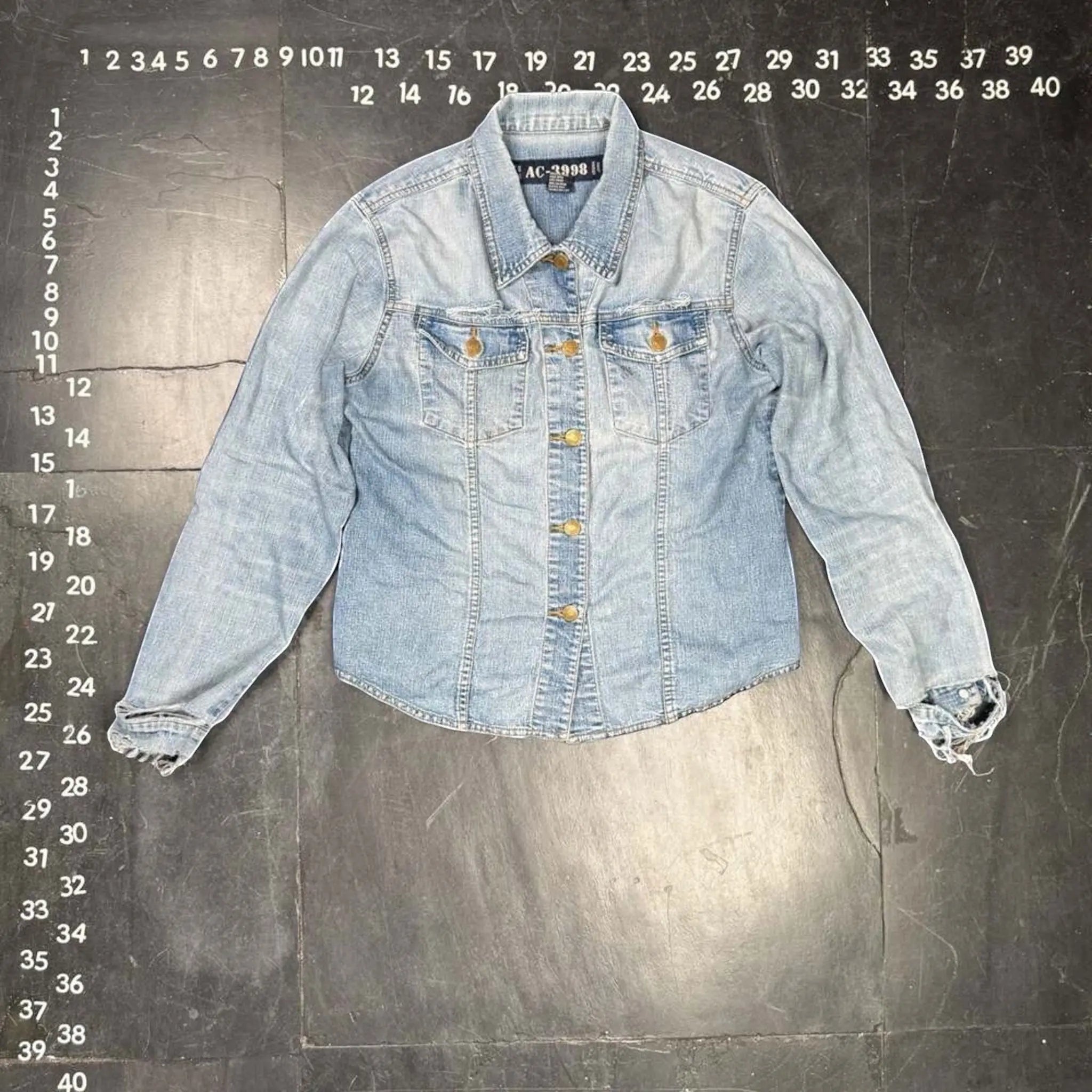 The Room Collective AC-3998 light wash denim trucker jacket with distressed cuffs and hem, gold-tone buttons, and dual chest pockets.